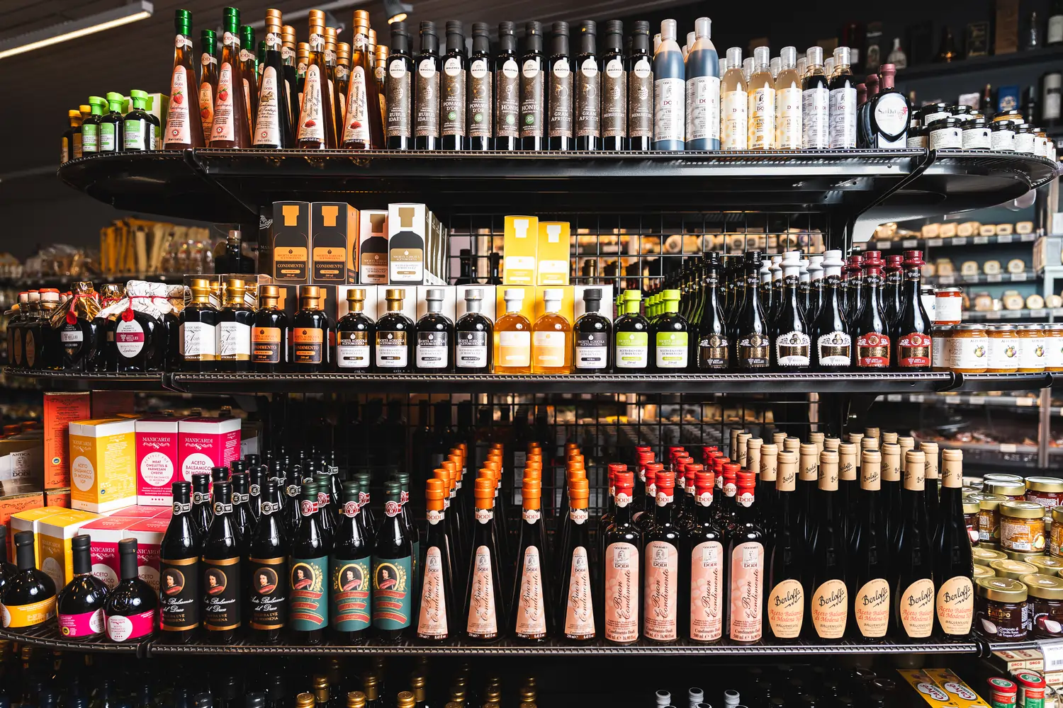 Das Bild zeigt ein Regal mit einer großen Auswahl an Balsamico Essigen.