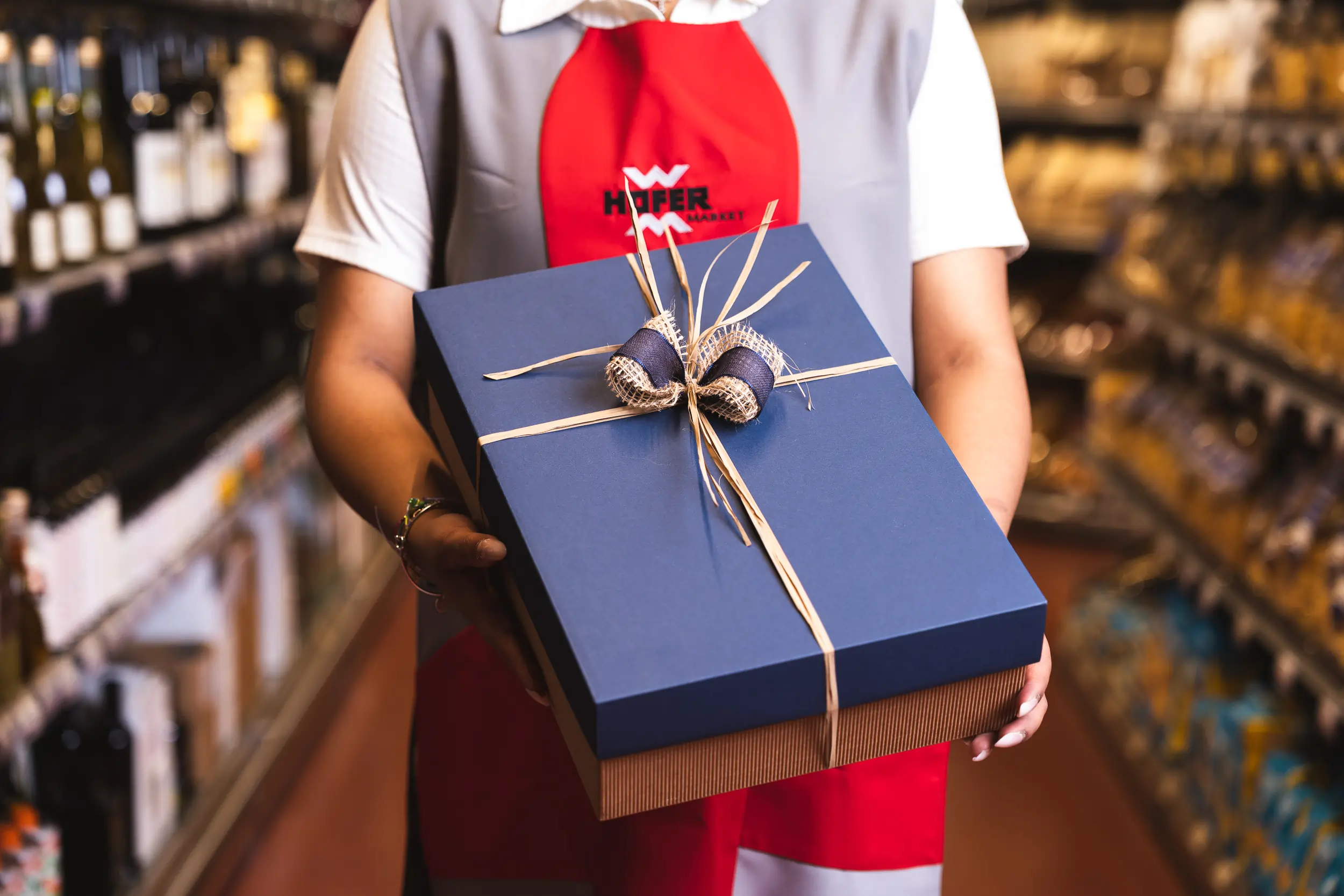 Eine Angestellte vom Hofer Market hält eine blaue Geschenkbox.