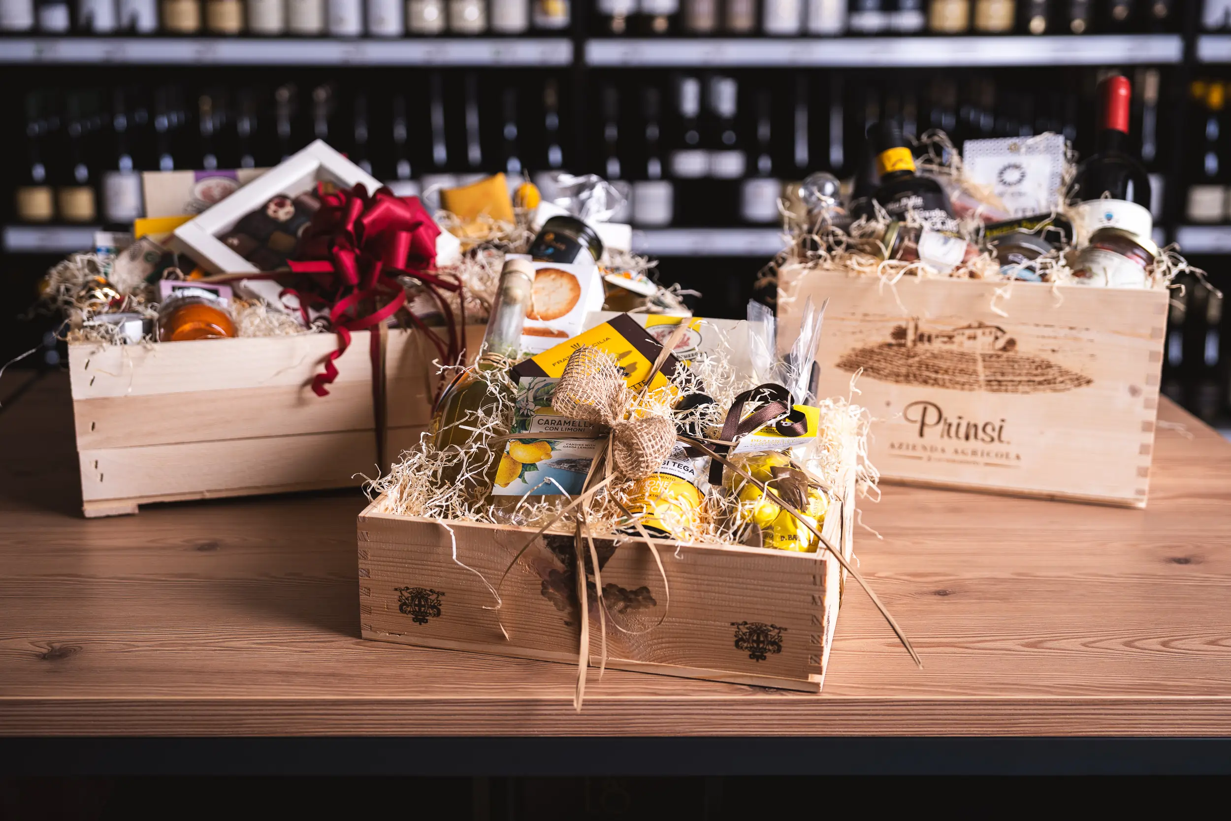 Man sieht drei verschiedene Geschenkkörbe aus Holz mit jeweils anderen Delikatessen. Alle sind optisch schön veriert.