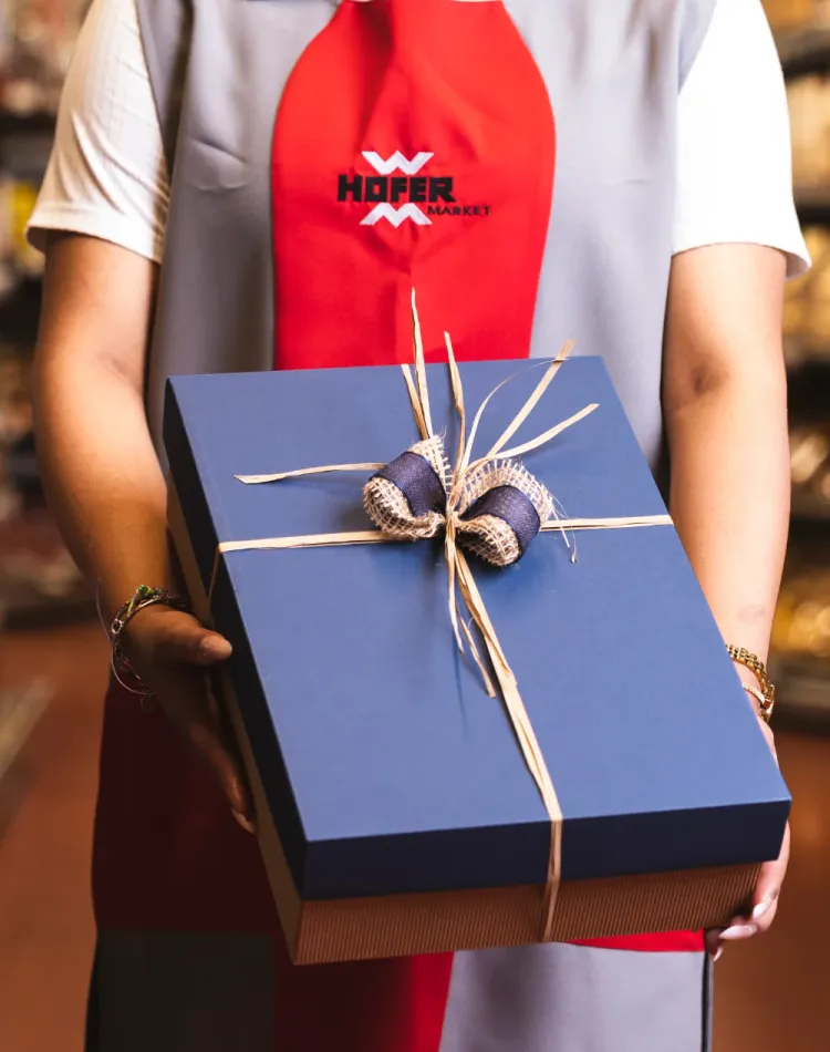 Eine Angestellte vom Hofer Market hält eine blaue Geschenkbox.