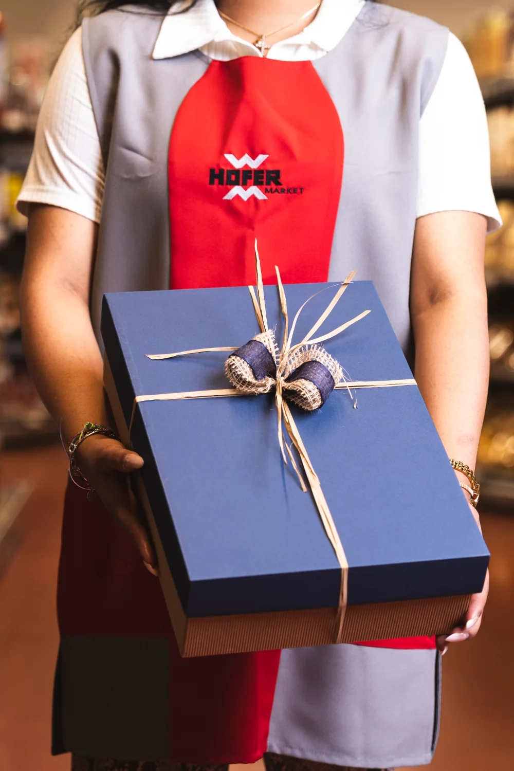 Eine Angestellte vom Hofer Market hält eine blaue Geschenkbox.