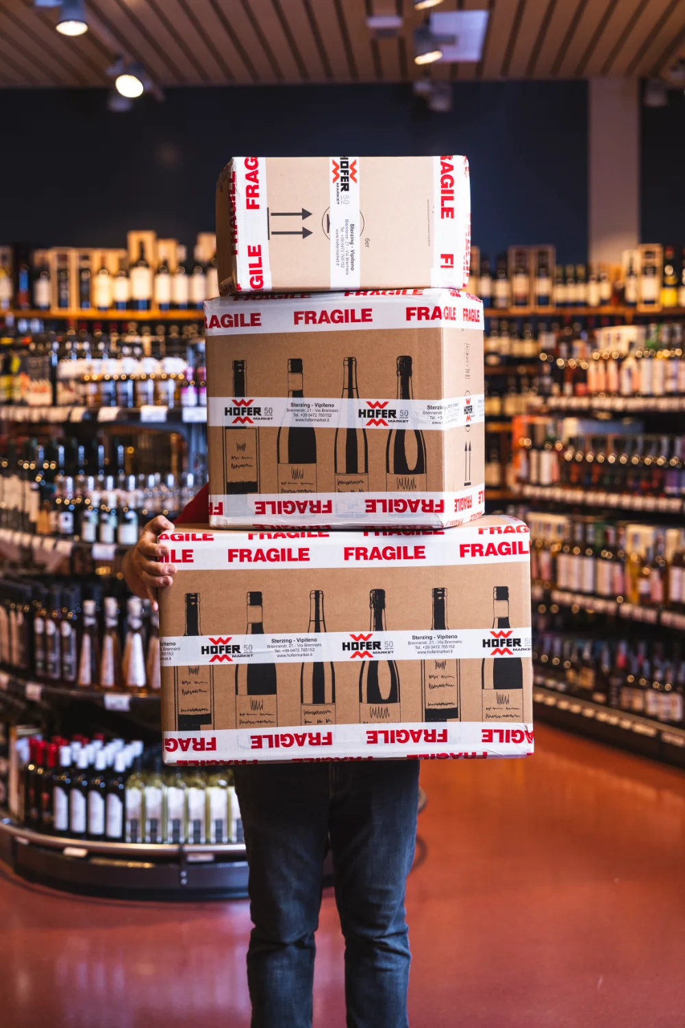 Ein Angestellter des Hofer Market hält drei aufgestapelte Versandboxen.