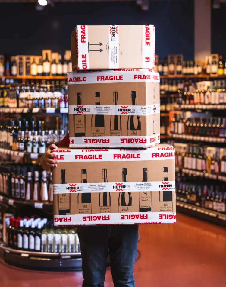 Ein Angestellter des Hofer Market hält drei aufgestapelte Versandboxen.