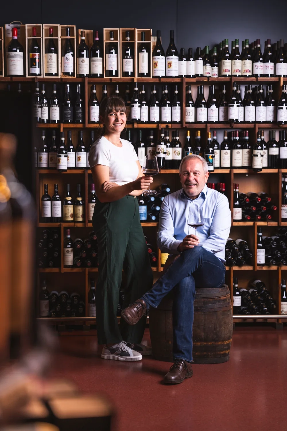 Sabine Hofer und Toni Hofer sind vor einem Weinregal und haben jeweils ein Glas Rotwein in der Hand.