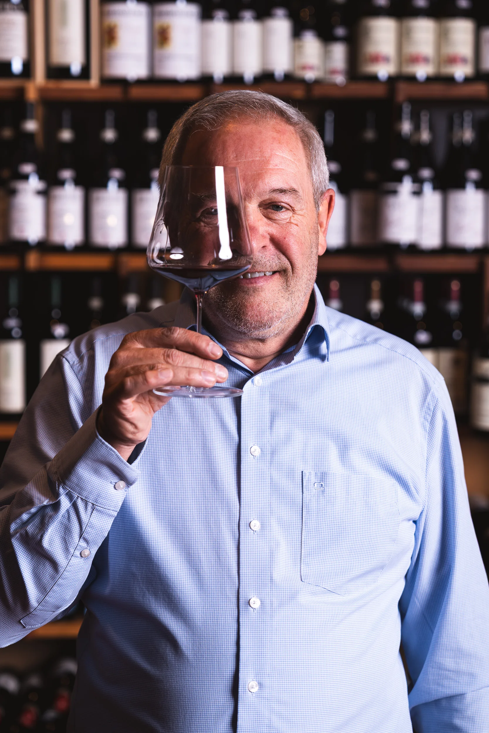 Toni Hofer sieht durch ein Weinglas in dem sich Rotwein befindet.