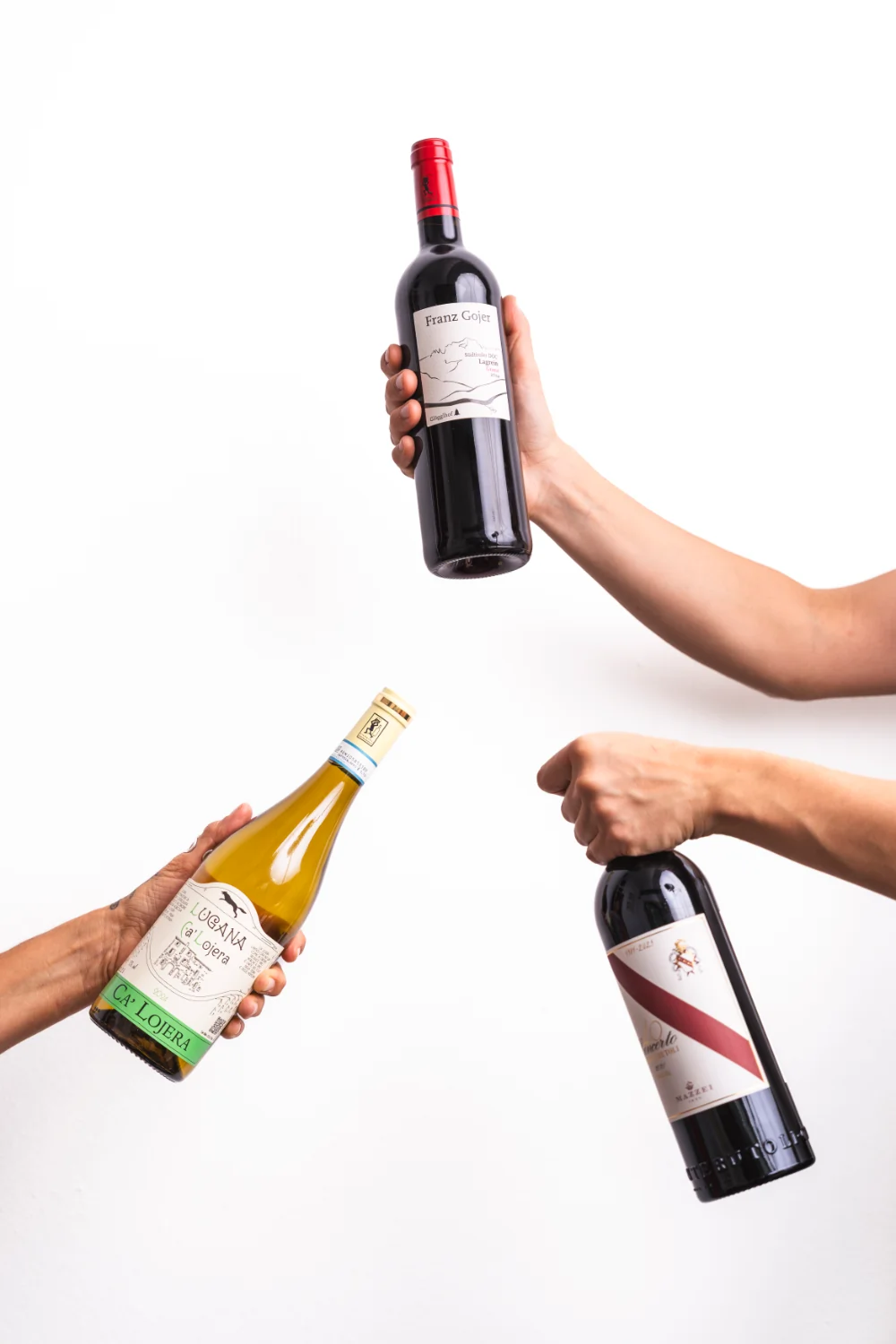 Drei Hände halten vor weißem Hintergrund jeweils eine Flasche Wein.